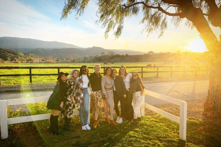 Group of people posing by a fence with a sunset view over hills and pasture.