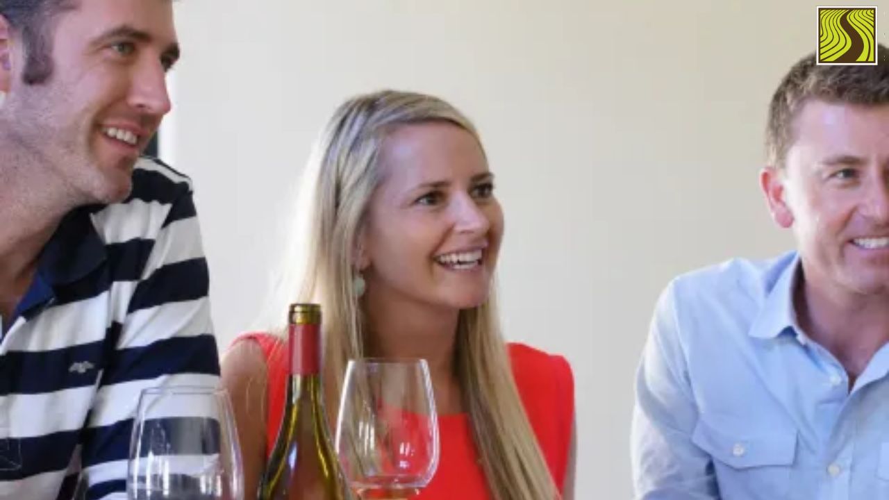 Three people smiling at a table with wine glasses and a wine bottle.