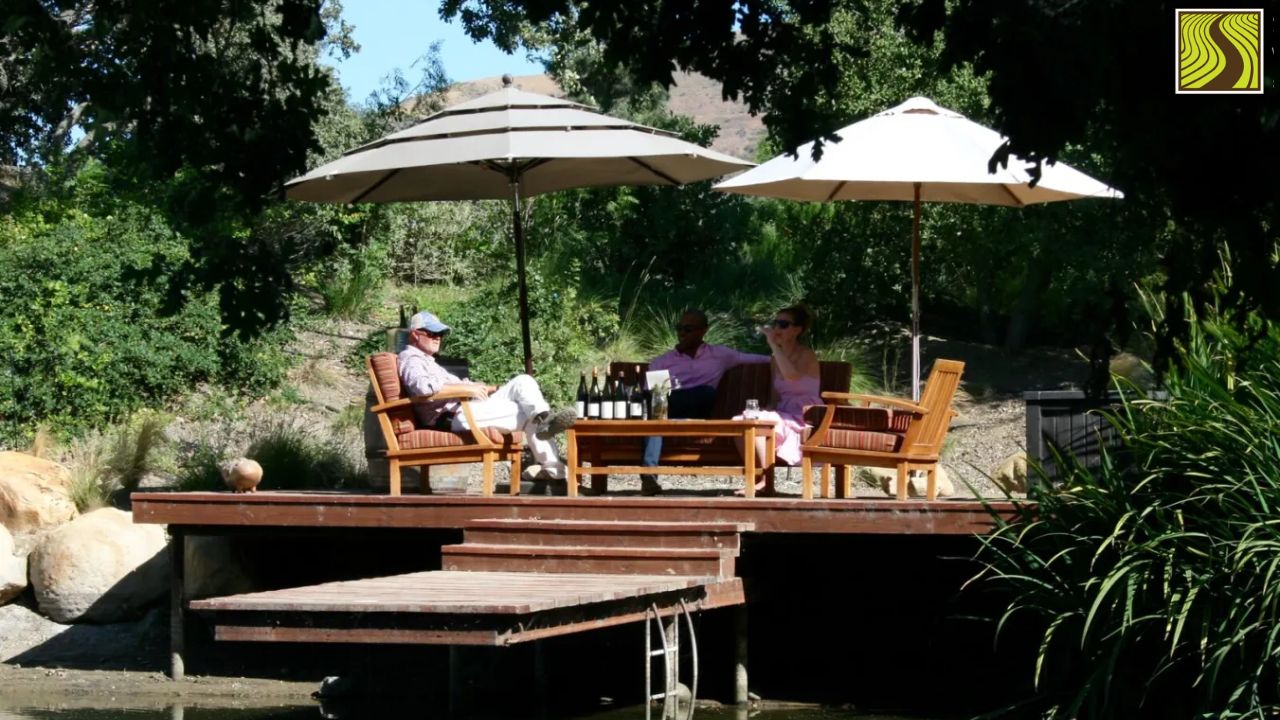 Three people sitting under umbrellas on a deck surrounded by trees and greenery.