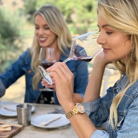 Two women in denim jackets enjoying red wine at an outdoor table.