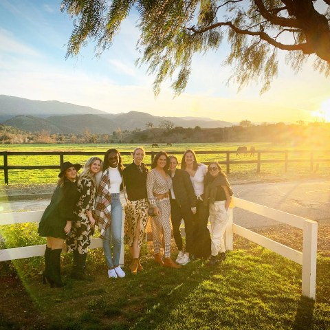 Group of women posing by a fence at sunset with mountains in the background.