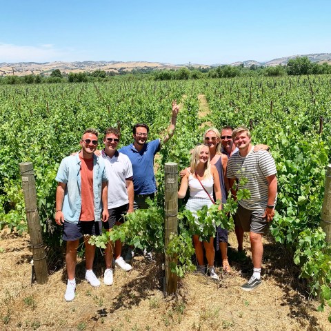 Group of people posing in a vineyard on a sunny day.