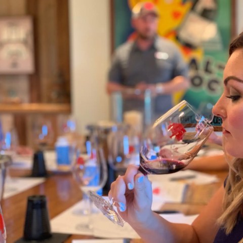 A woman smelling wine in a glass at a tasting event with people in the background.