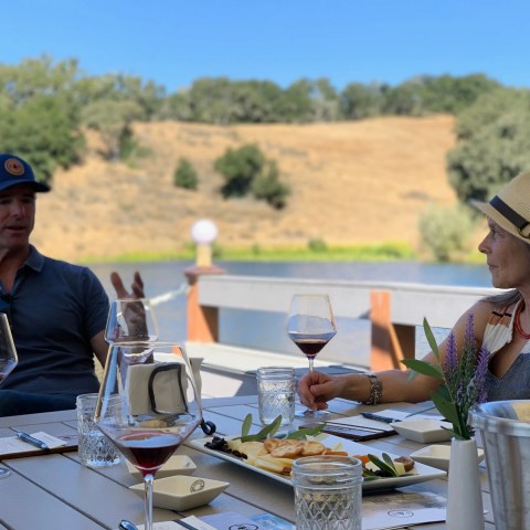 Two people sitting outdoors at a table with wine glasses, talking with a scenic view.