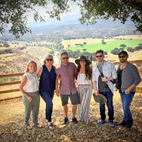 Group of six people posing in front of a scenic landscape with trees and mountains.