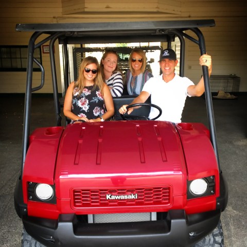 Four people sitting in a red Kawasaki utility vehicle inside a garage.