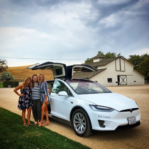 Three people beside a white car with open doors, barn and cloudy sky in background.