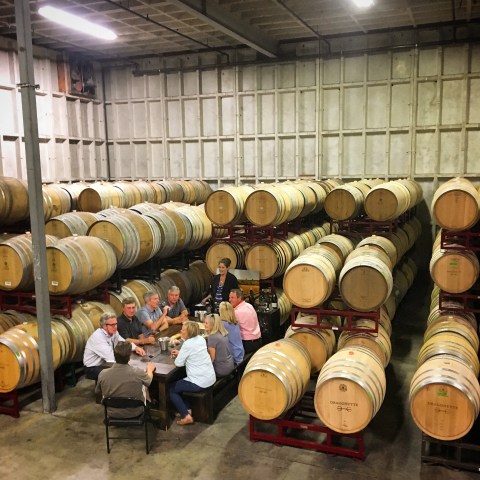 Group sitting at table in a wine cellar surrounded by wooden barrels.