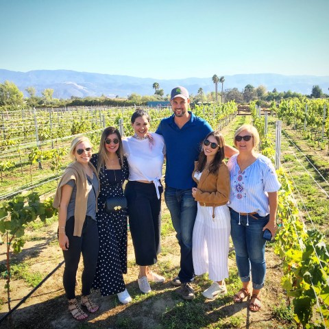 Group of people smiling in a vineyard with mountains in the background.