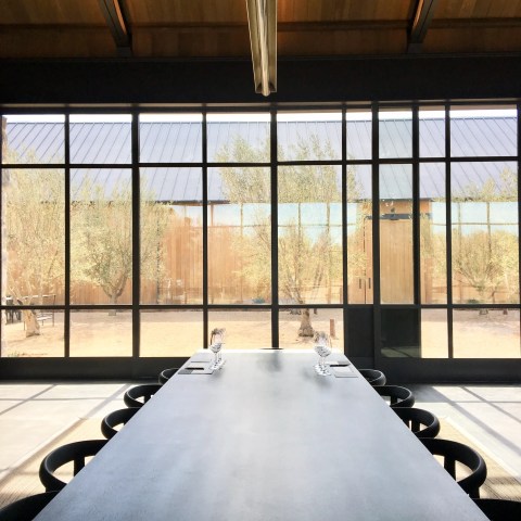 Long table set with glasses, window with a view of trees and a building outside.
