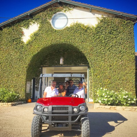 People in a red utility vehicle in front of an ivy-covered building under a clear blue sky.