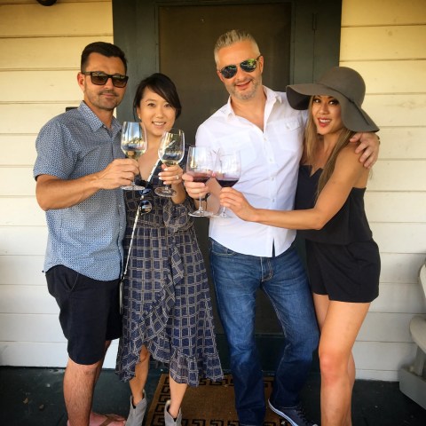 Four people smiling and toasting with wine glasses on a porch.