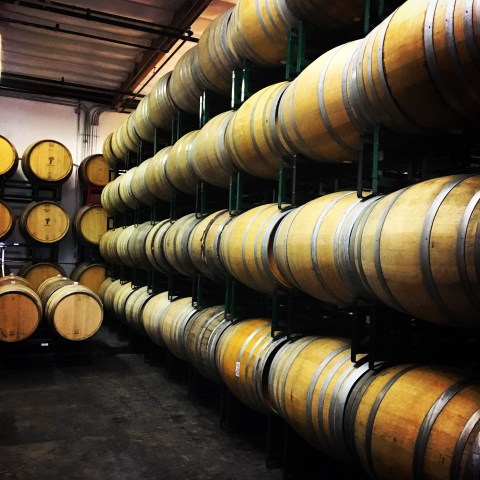 Stacks of wooden barrels in a dimly lit warehouse.