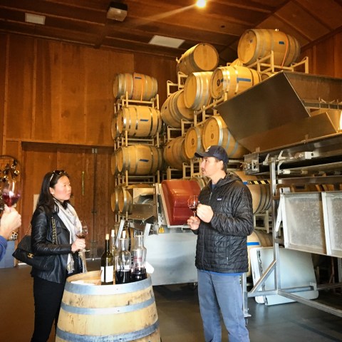 Three people tasting wine in a winery with barrels in the background.