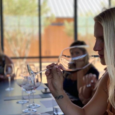 Woman tasting wine at a table with others, holding a wine glass, focused.