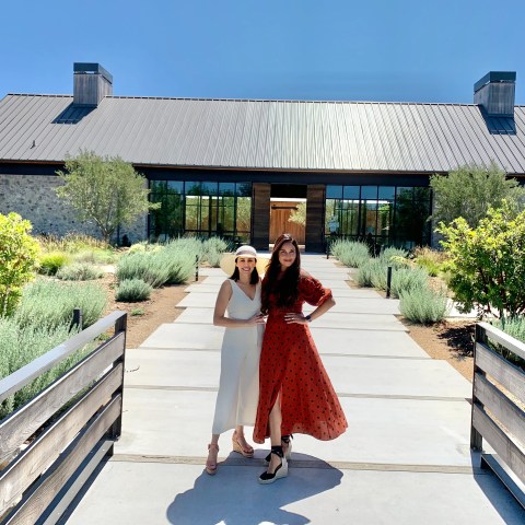 Two people posing in front of a modern building with a pathway and garden.