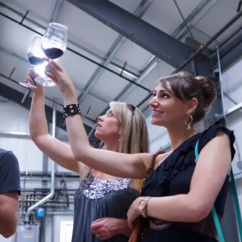 Three people examining wine glasses in an industrial setting.