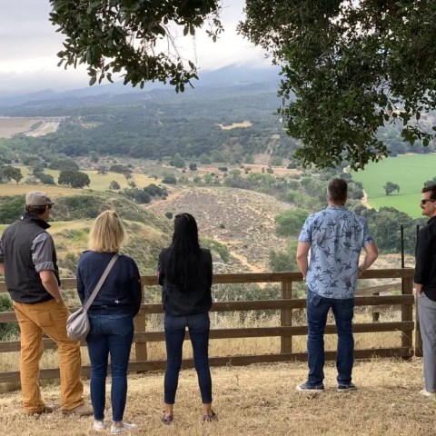Five people standing on a hilltop overlooking a scenic landscape with trees and fields.