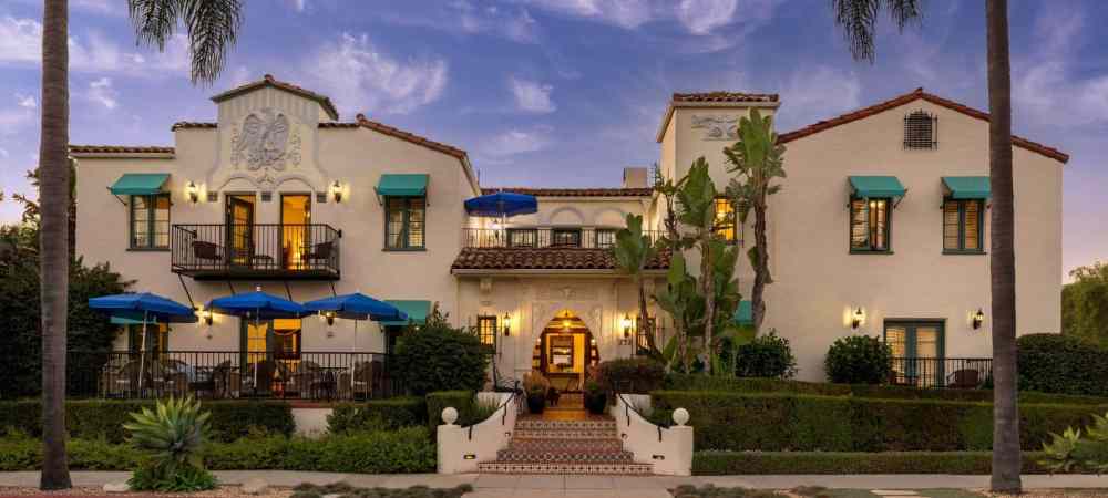 Mediterranean-style building with blue awnings and palm trees at dusk.