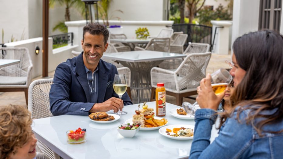 People dining outdoors, smiling and enjoying drinks and snacks at a table.
