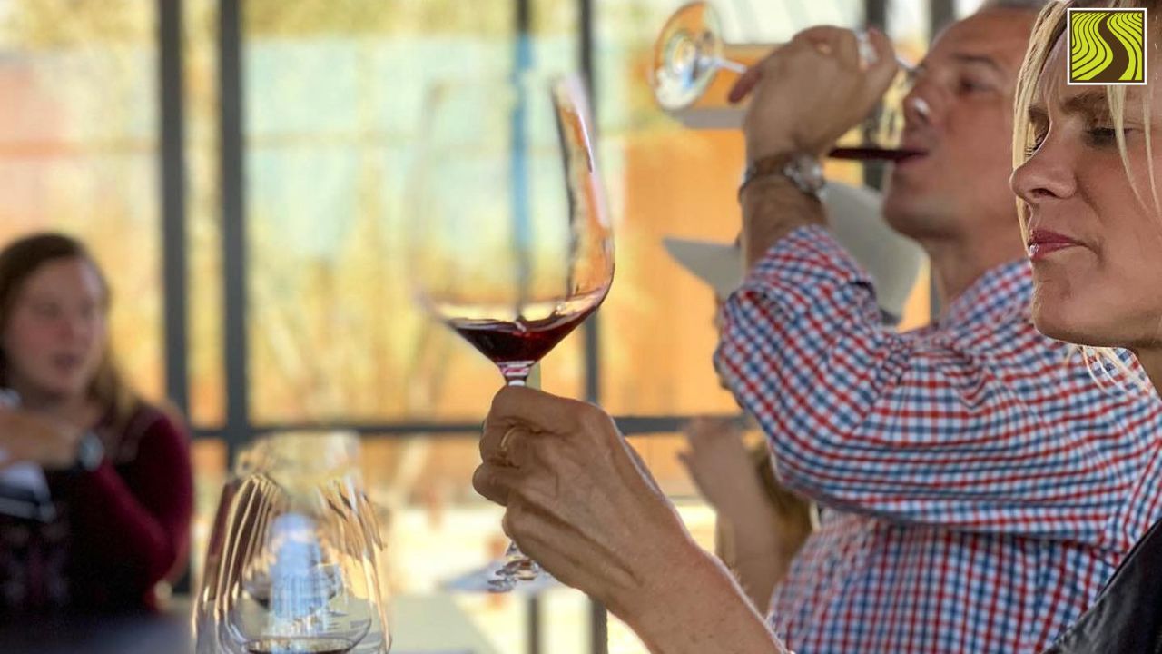 People tasting wine at a table with glasses in focus and blurred background.