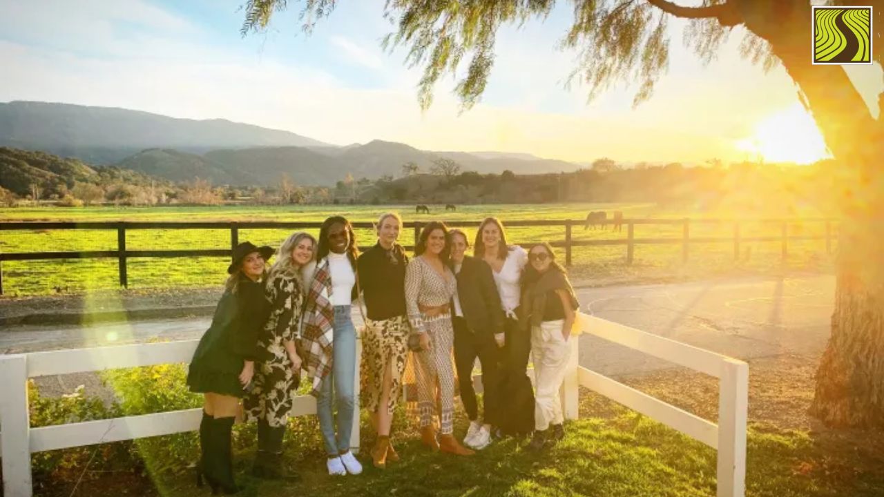 Group of seven people posing by a white fence with a scenic sunset and mountains in the background.