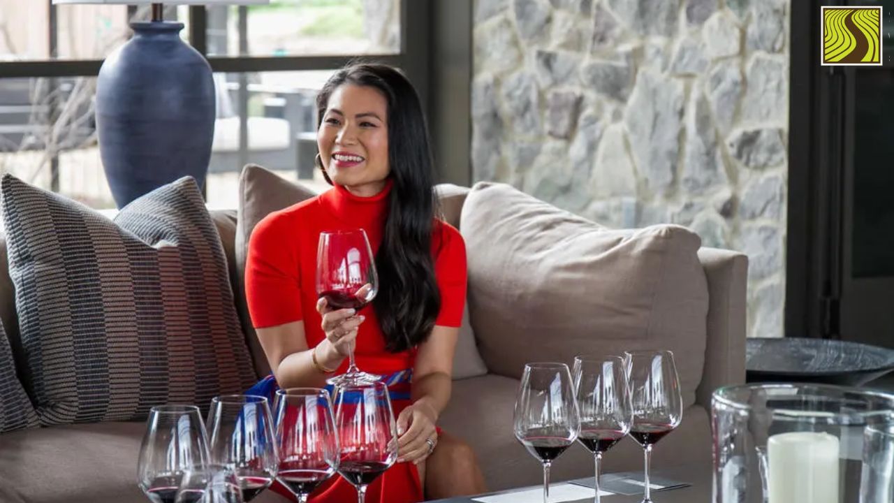 Woman in red dress holding wine glass, sitting on sofa with wine glasses on table.