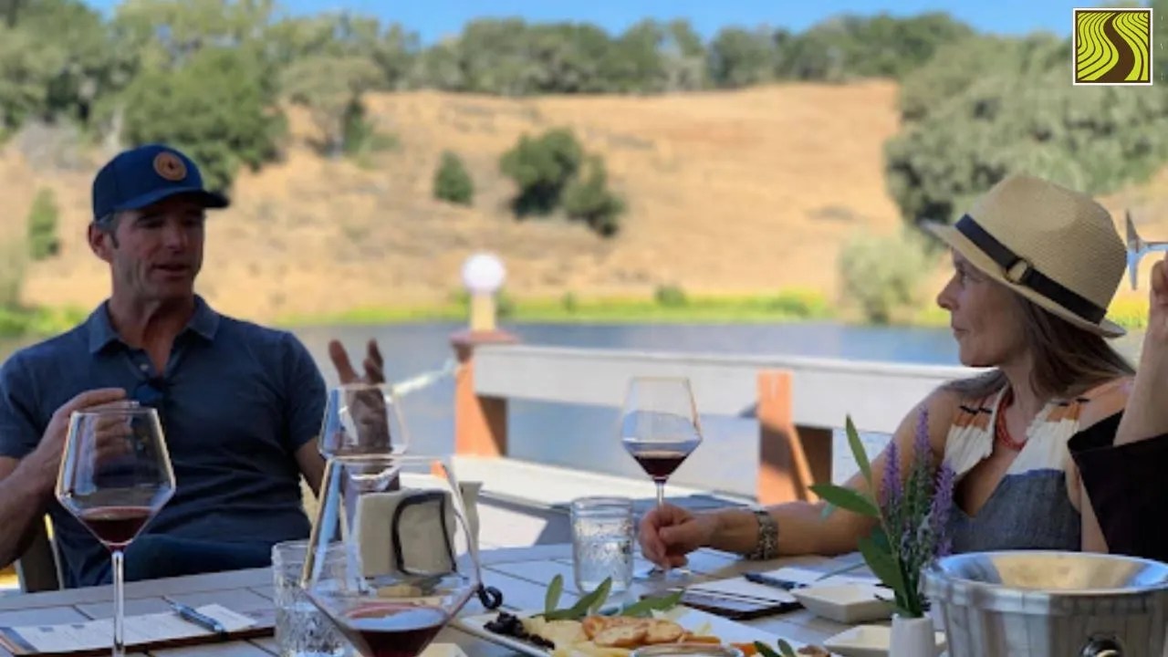 Two people sitting at an outdoor table with wine glasses and snacks, engaging in conversation.