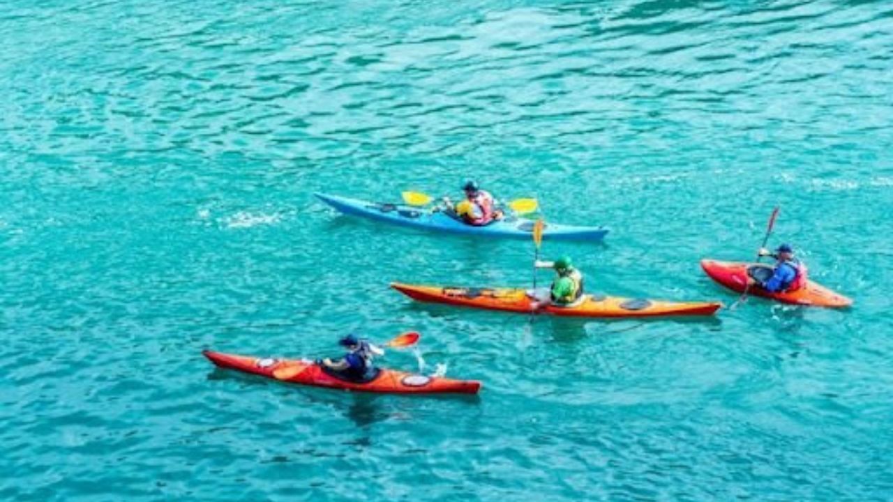 Four people kayaking in bright kayaks on turquoise water.