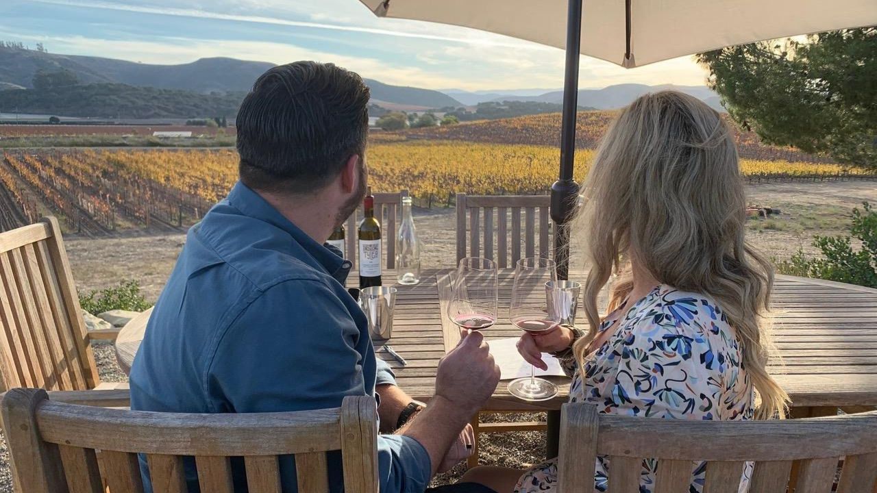 Couple enjoying anniversary wine tour overlooking autumn vineyard hills.