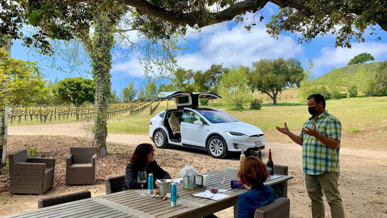 Outdoor wine tour with guide, tasting setup, and Tesla nearby in the vineyard.
