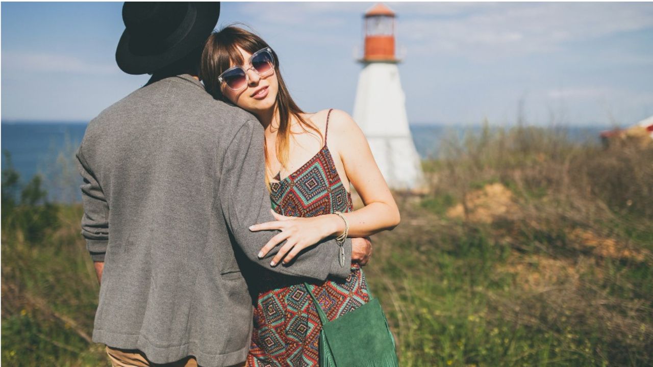 Couple standing near California lighthouse with scenic coastal backdrop.