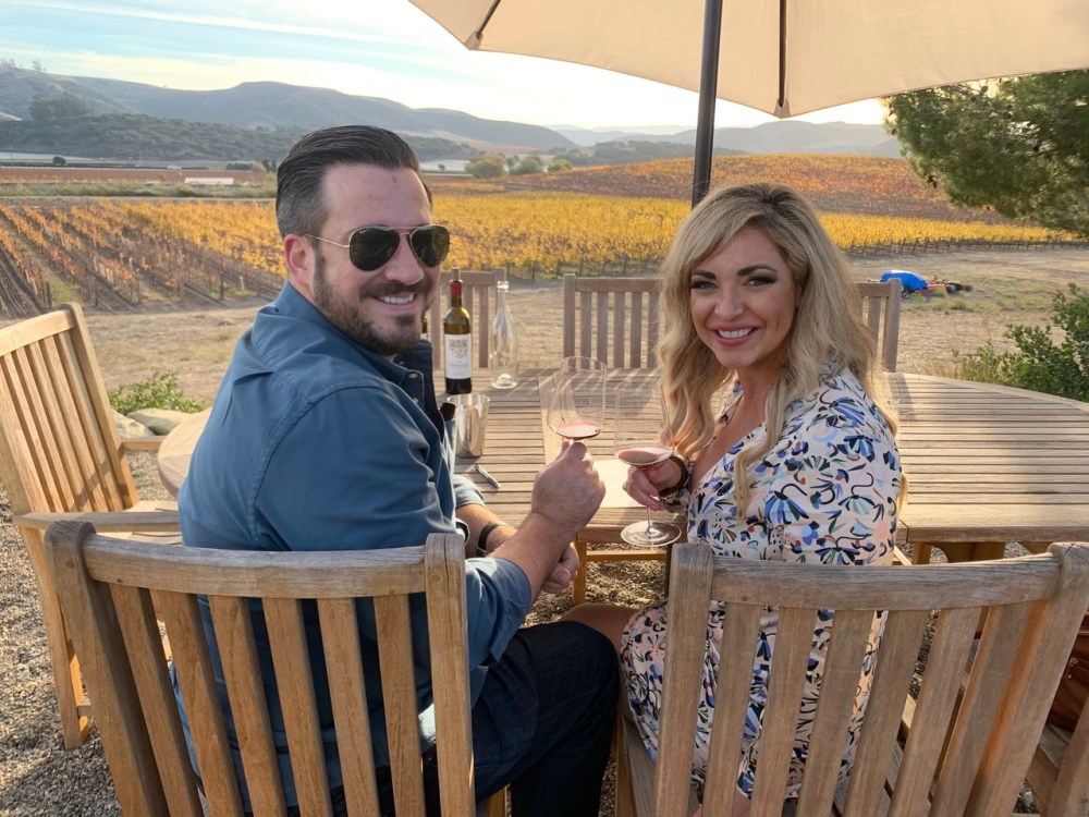 Couple enjoying private wine tour overlooking vineyard at sunset​‌